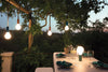 Fermob Aplo outdoor lights hanging from trees and on an outdoor table.
